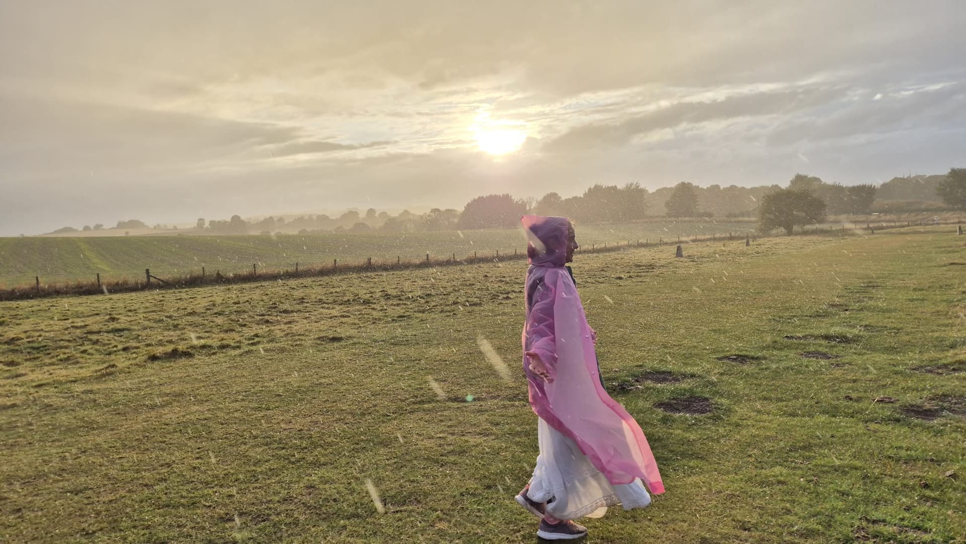Priestess in flowing pink cloak walking through misty fields at golden hour